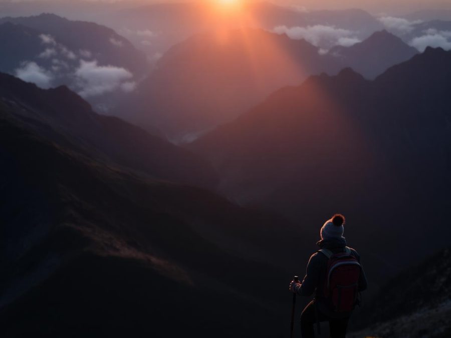 Hiker with a red backpack on a rocky summit at sunrise