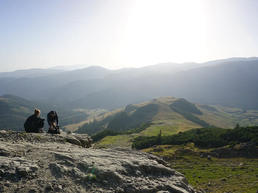 Two walkers resting on a rock outcrop, looking out across ridges into the haze